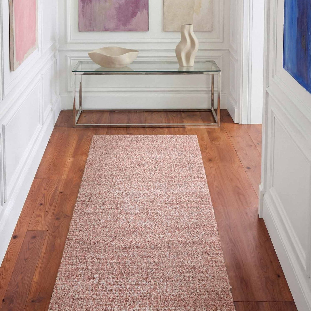 Long rectangular rug on a wooden floor with a glass table and decorative items in the background.