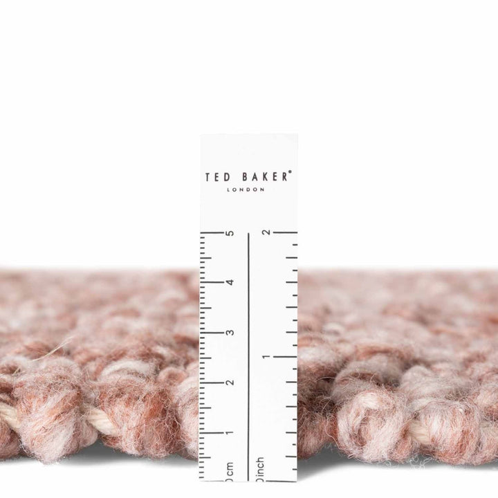 Close-up of pink textured fabric with a ruler and 'Ted Baker London' branding.