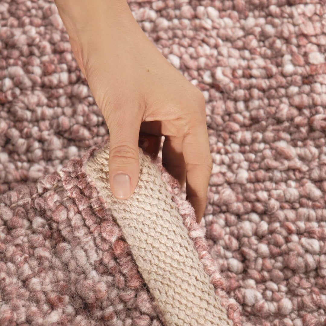 Hand holding a carpet sample against a textured pinkish-brown carpet background