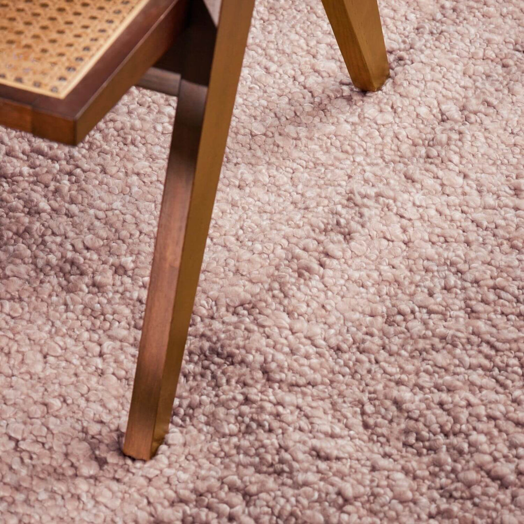 Close-up of a wooden chair leg on a textured pink carpet