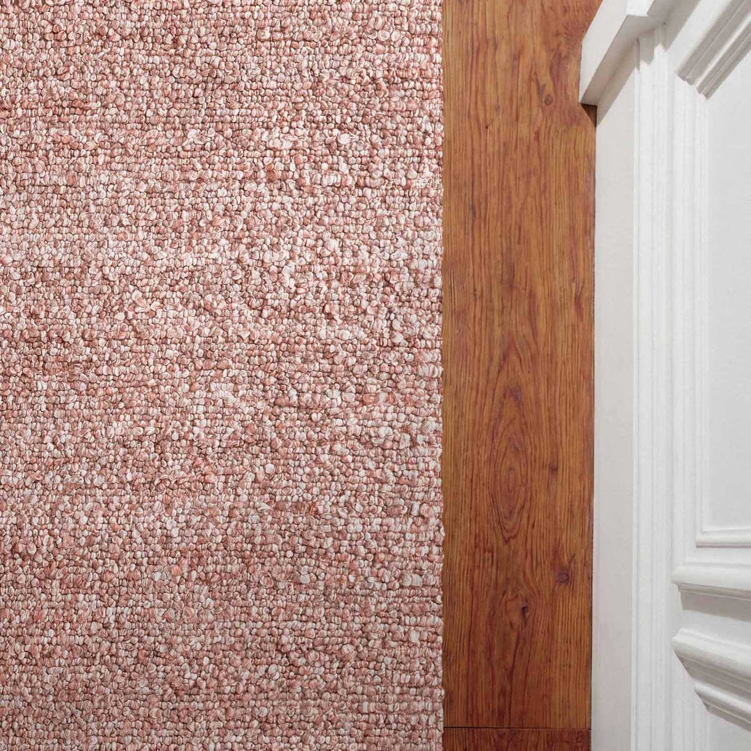 Close-up of a carpeted floor transitioning to a wooden floor with a white baseboard.