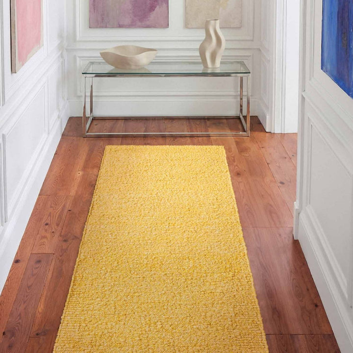 Yellow runner rug on a wooden floor with a glass table and decorative items in the background.