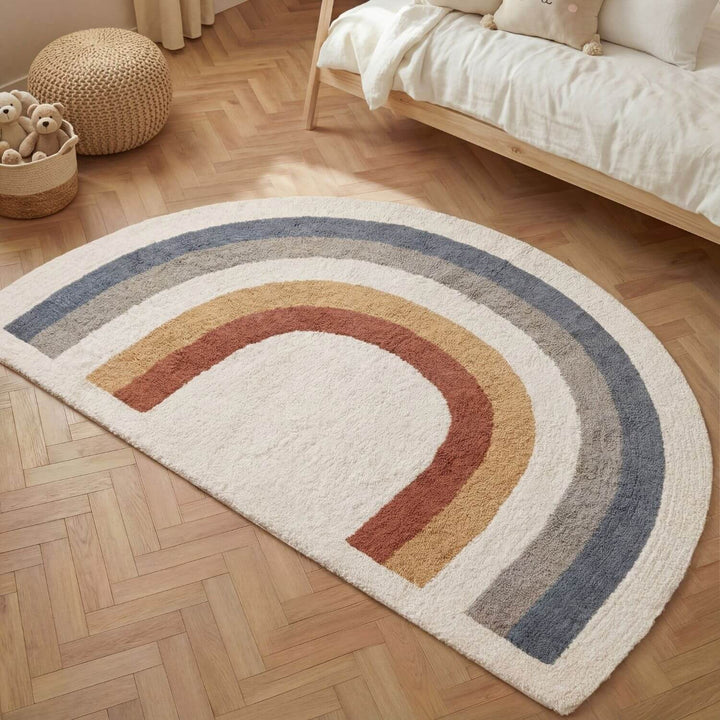 Rainbow-shaped rug on a wooden floor with a bed and toys in the background