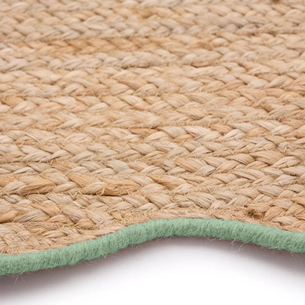 Close-up of a woven natural fiber rug with a green border on a white background