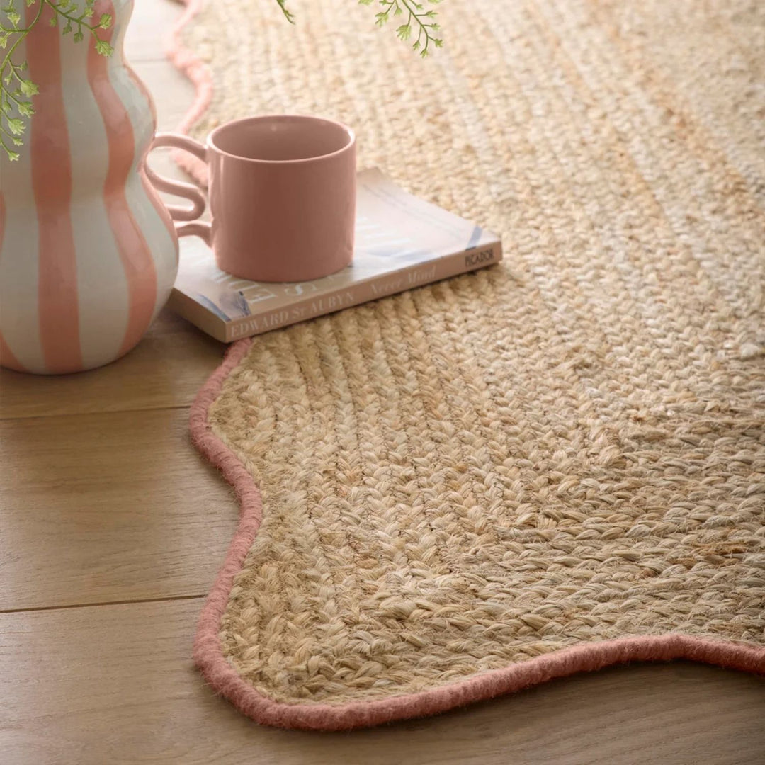 Natural fiber rug with a pink mug and striped vase on a wooden floor
