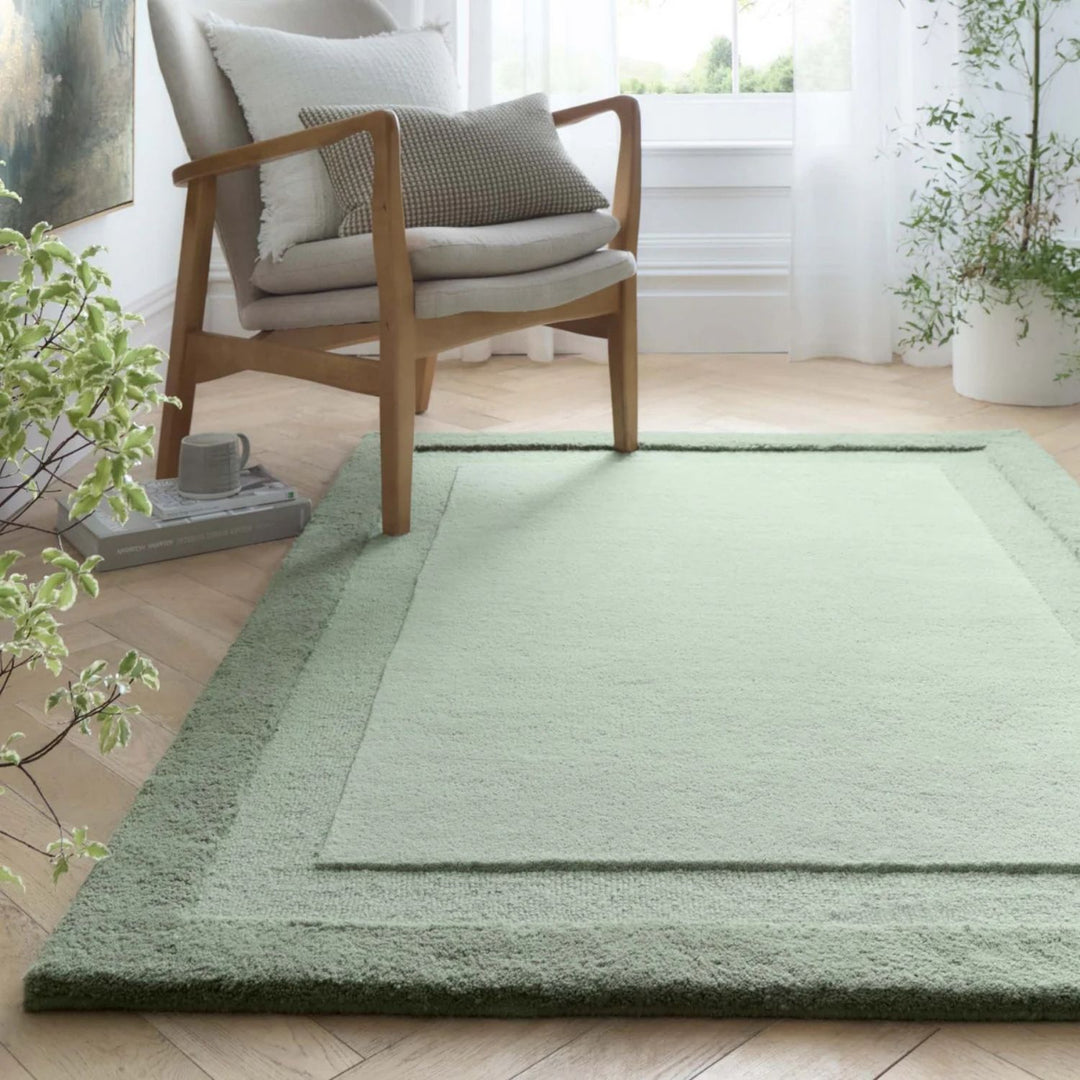 Green rug on a wooden floor with a chair and plants in a room.