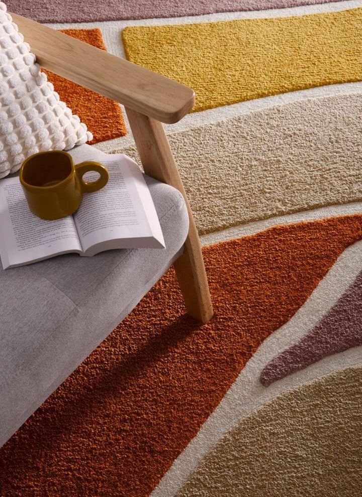 Strata Abstract Rug with deep pile in warm Terra colorway, styled near a cozy chair with a book and mug.