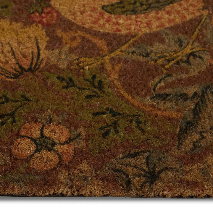 Close-up of a doormat with autumn-themed design featuring pumpkins and leaves.