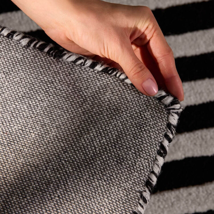 Hand holding a gray fabric with black trim against a striped background