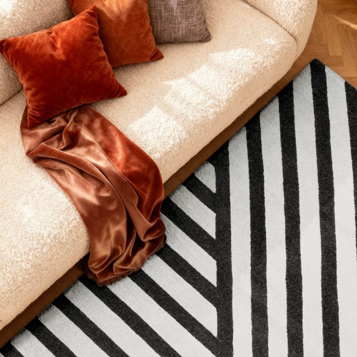 Beige sofa with orange cushions and a blanket on a black and white striped rug.