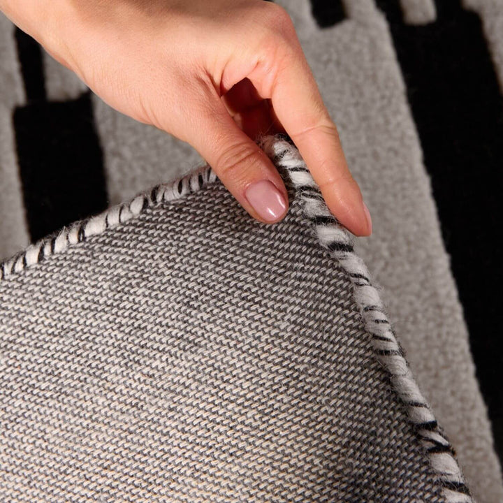 Hand holding a textured gray fabric with a patterned edge