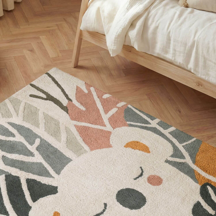 Decorative rug with a cartoon character on a wooden floor next to a bed.