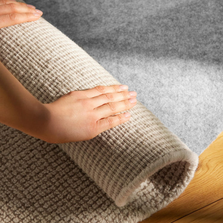 Person rolling out a beige carpet on a gray floor