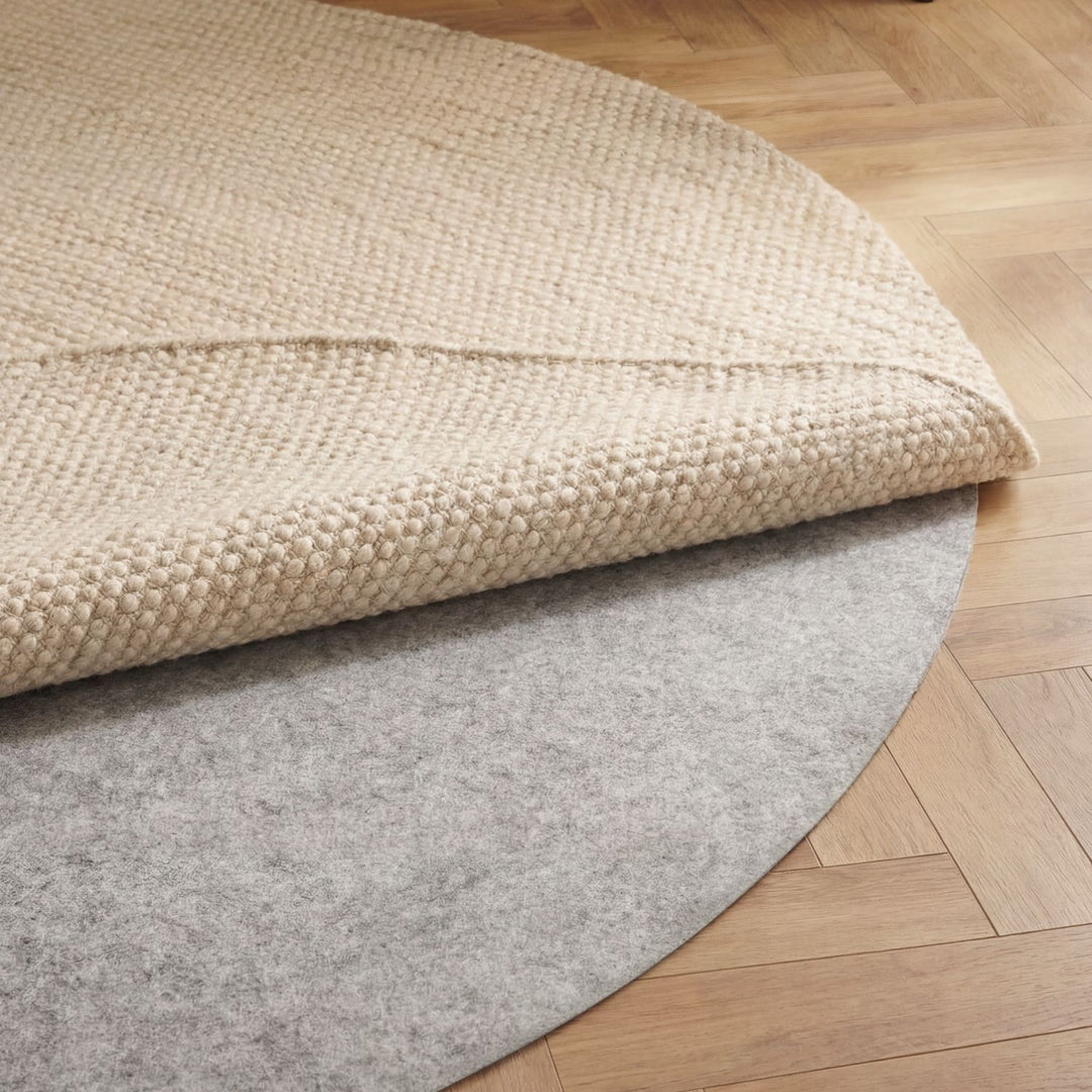 Beige textured rug partially unrolled on a wooden floor with gray underlay.