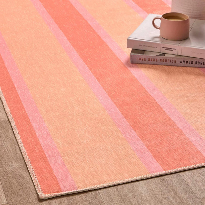 Striped pink and orange rug on a wooden floor with books and a mug.
