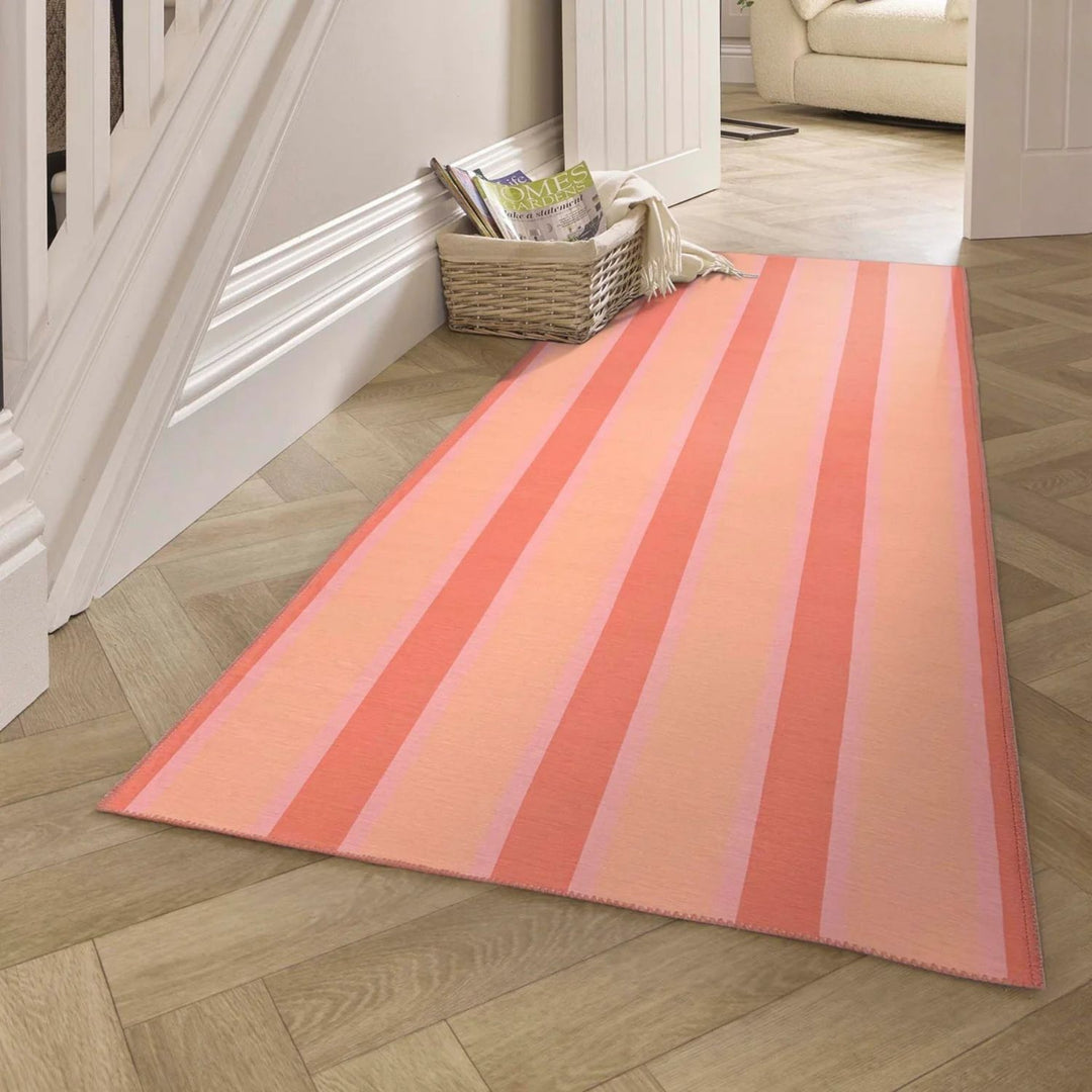 Striped pink and orange rug on a wooden floor with a white staircase in the background.
