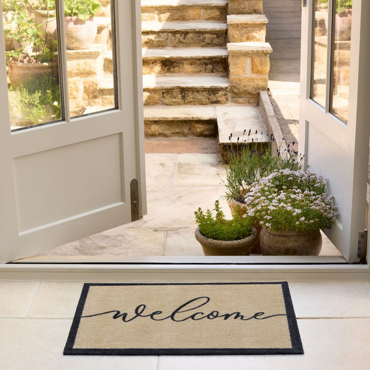 Welcome mat in front of a door with plants and steps leading outside