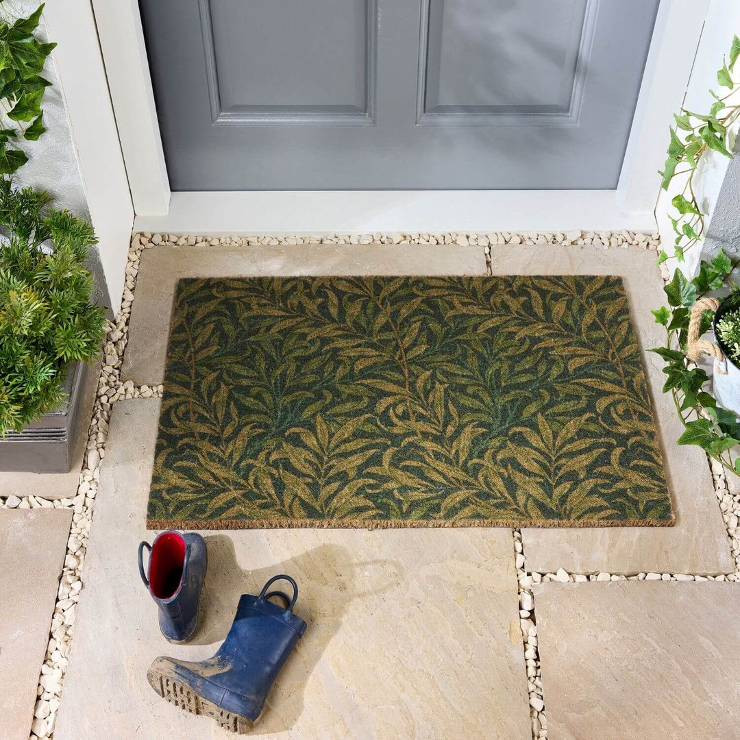 Doormat with leaf pattern on a stone patio in front of a gray door.