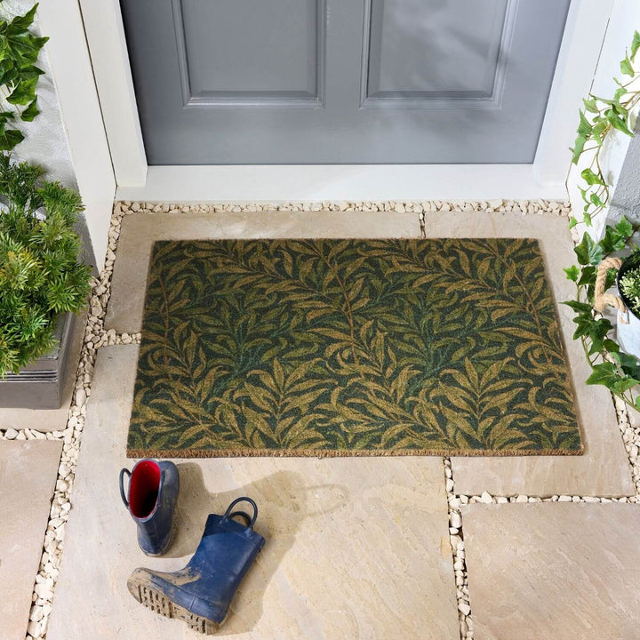 Doormat with leaf pattern on a stone patio in front of a gray door.