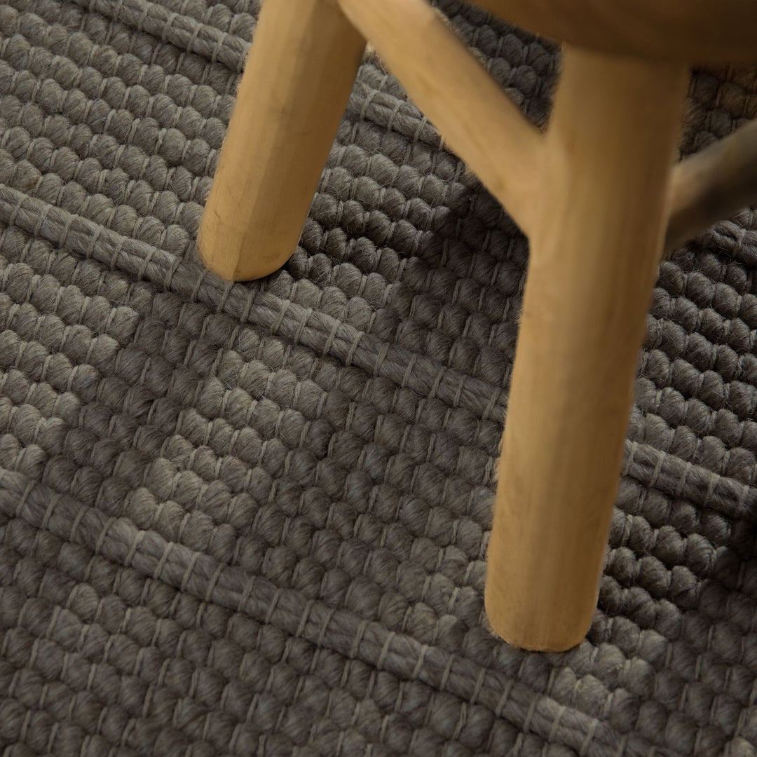 Close-up of a wooden chair leg on a textured gray carpet
