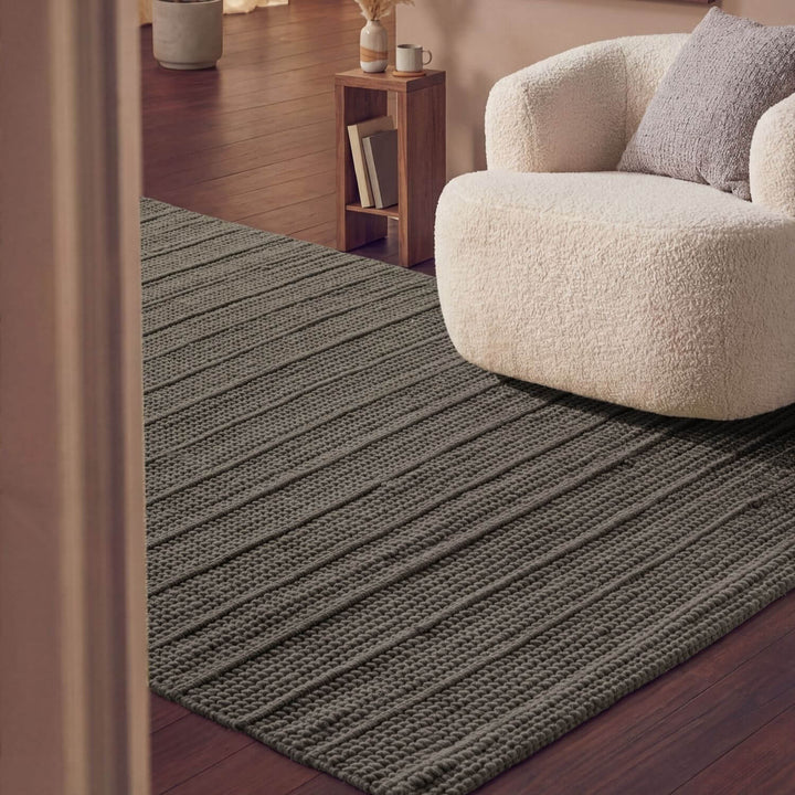 Gray striped rug on a wooden floor with a beige armchair and small wooden table in the background.