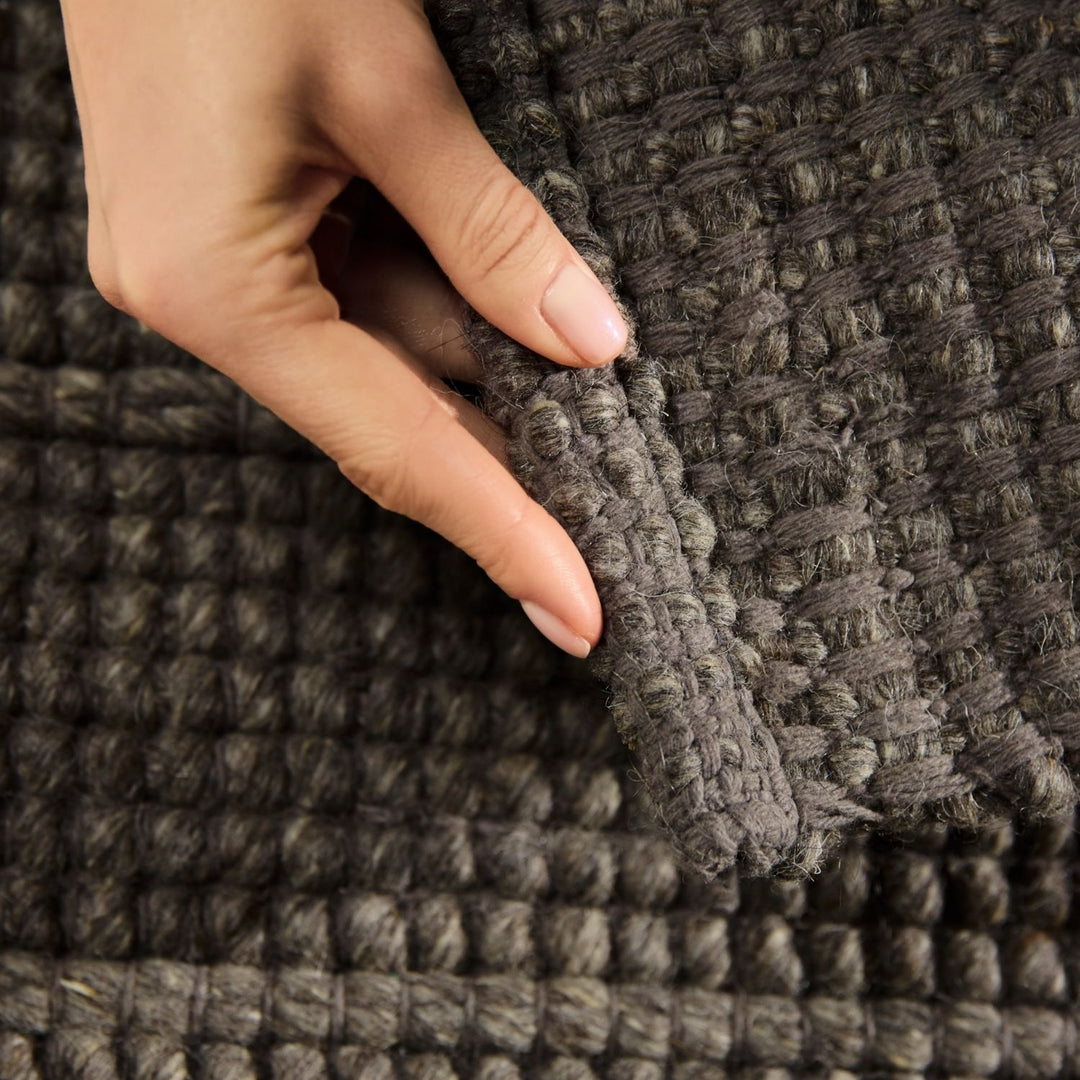 Hand touching a textured gray fabric surface