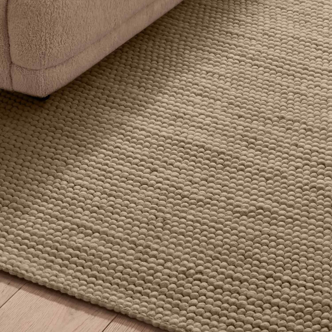 Close-up of a textured beige rug on a wooden floor.