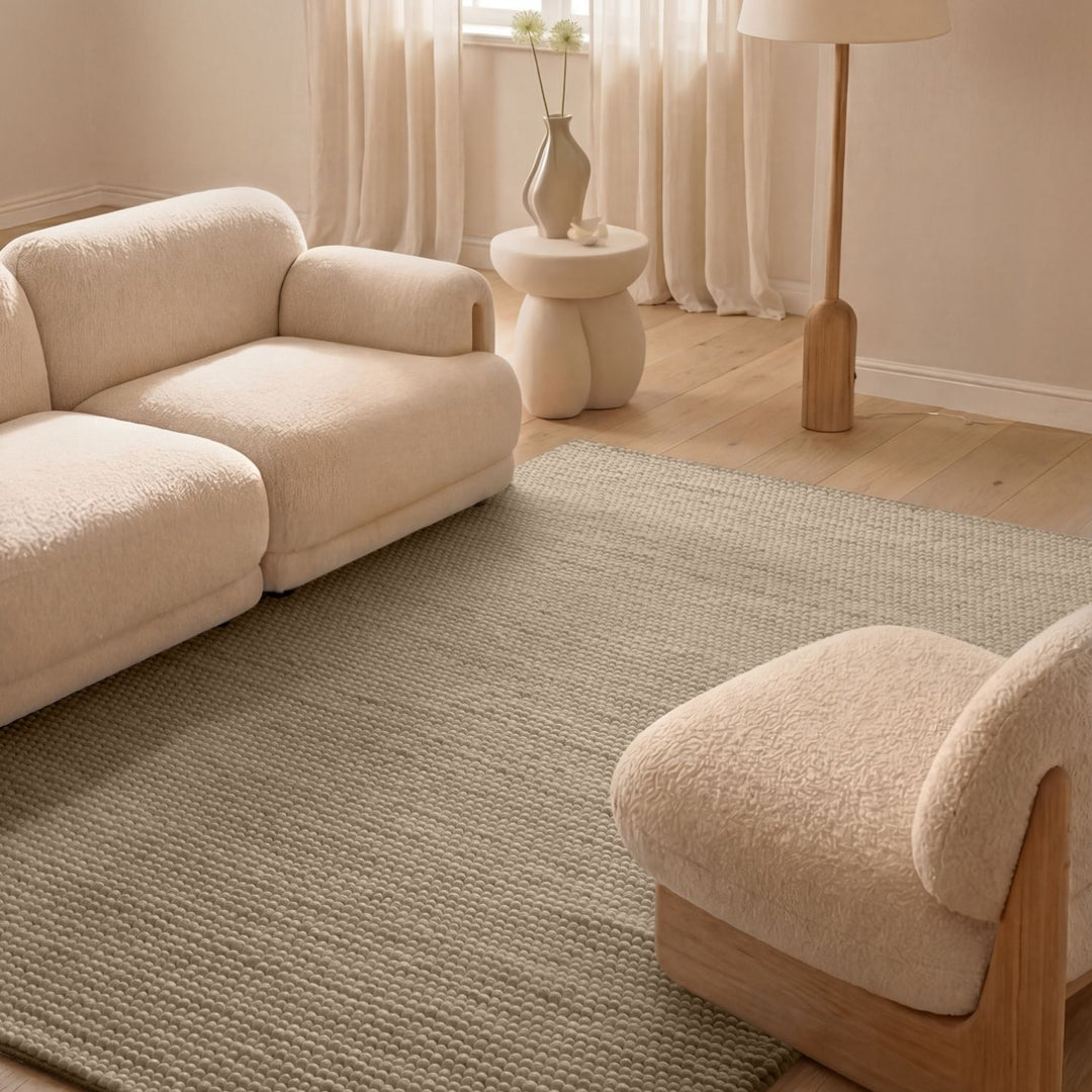 Beige sofa and chair in a living room with a textured rug and lamp.