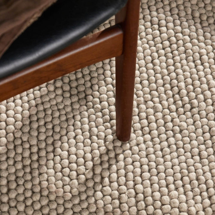 Close-up of a textured beige carpet with a wooden chair leg.