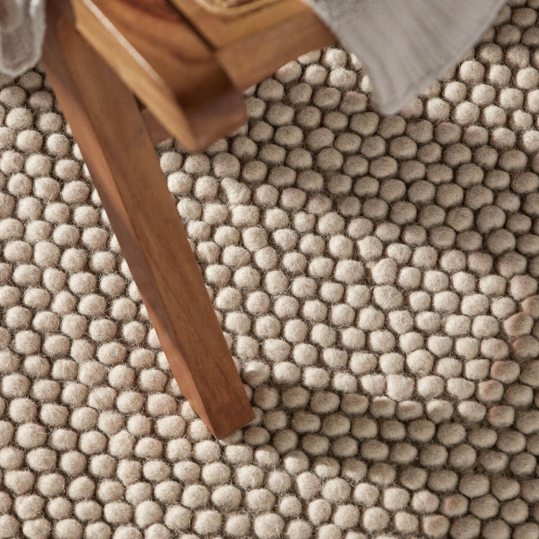 Close-up of a textured beige carpet with wooden furniture leg.