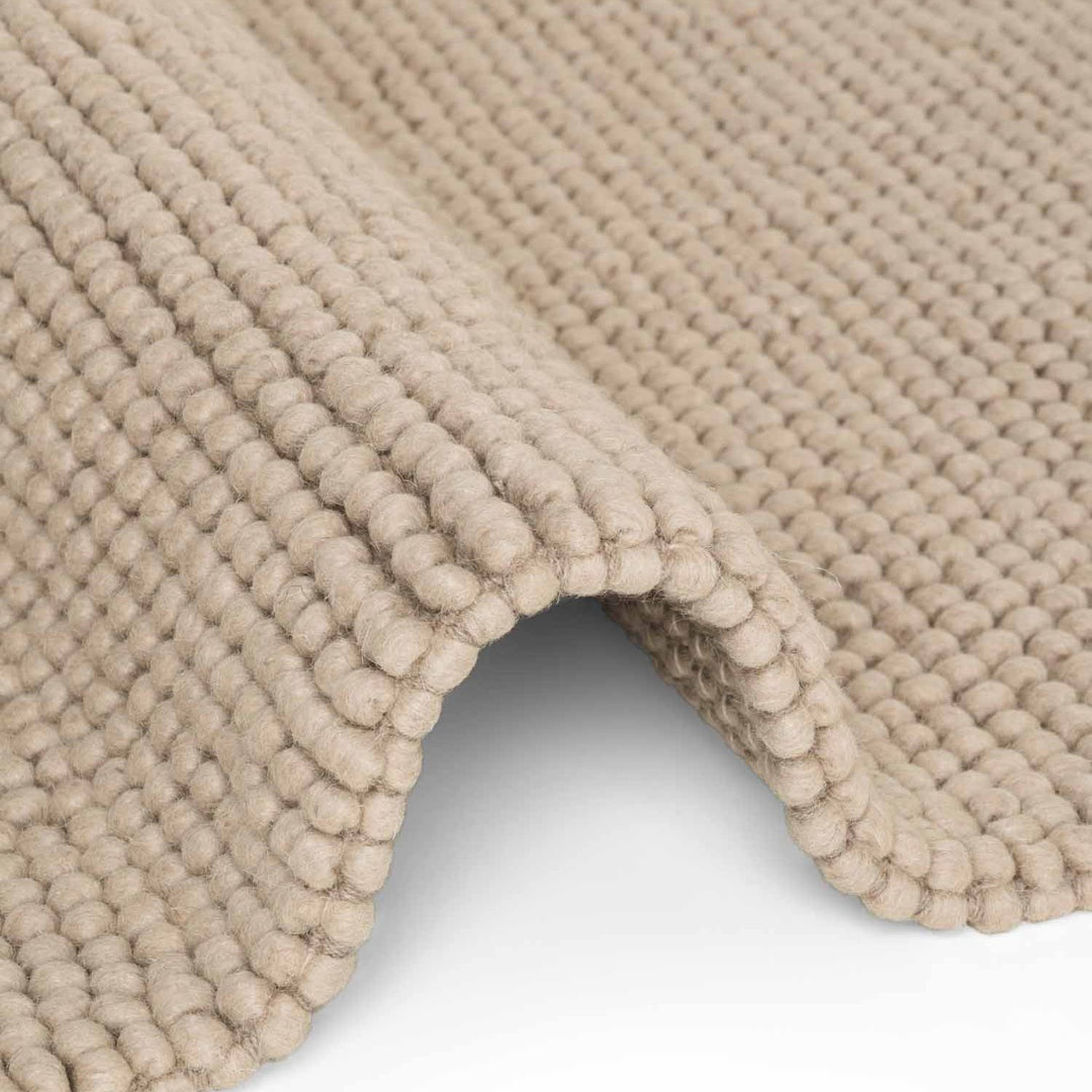 Close-up of a beige textured rug corner on a white background