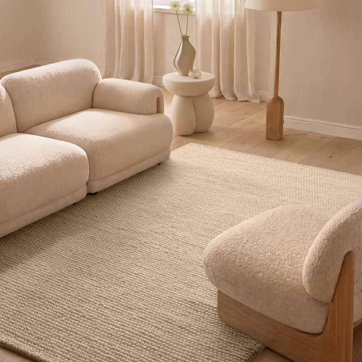 Beige sofa and armchair in a living room with a textured rug and neutral decor.