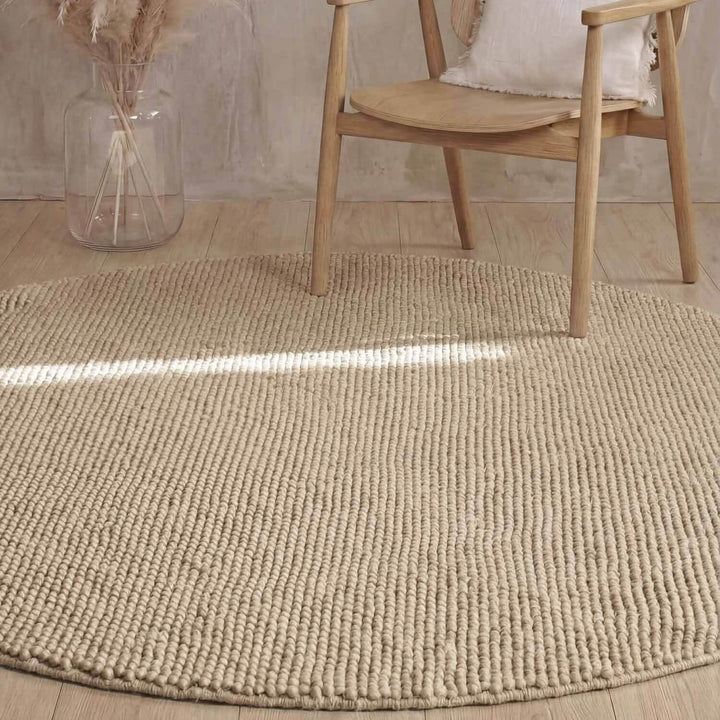 Beige textured rug on a wooden floor with a wooden chair and decorative elements.
