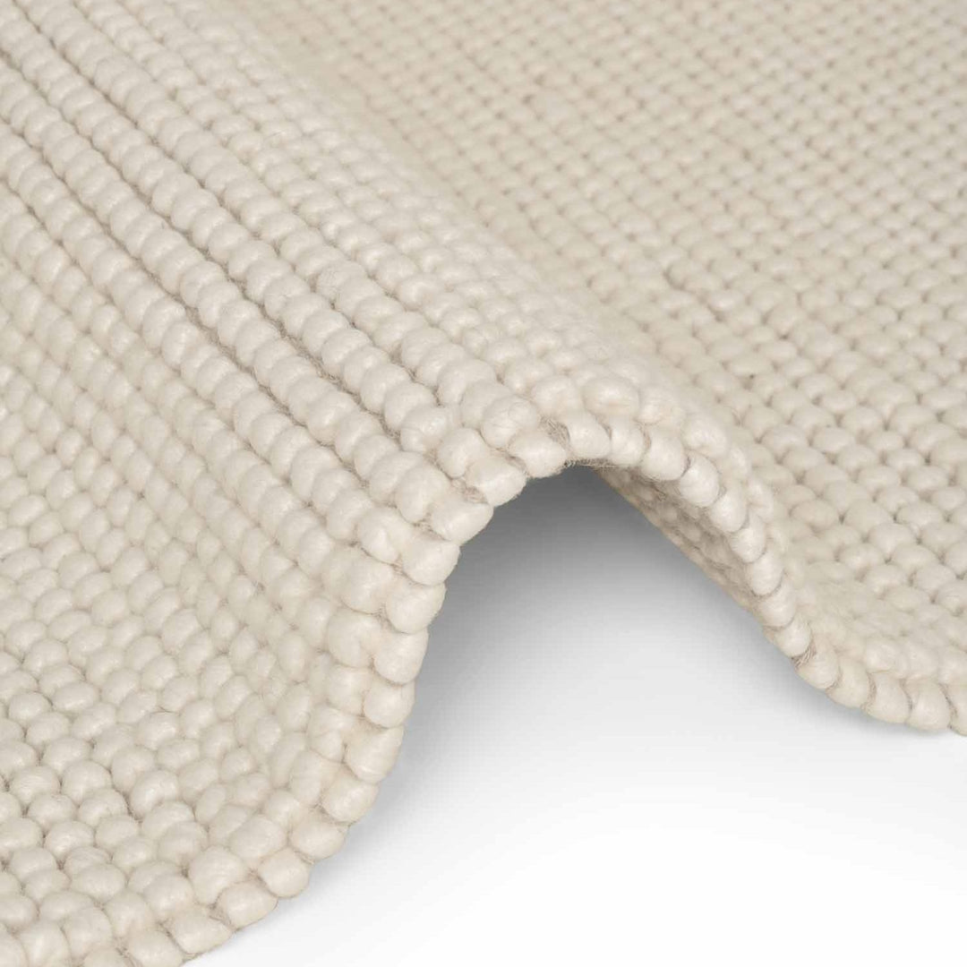 Close-up of a textured beige rug corner on a white background