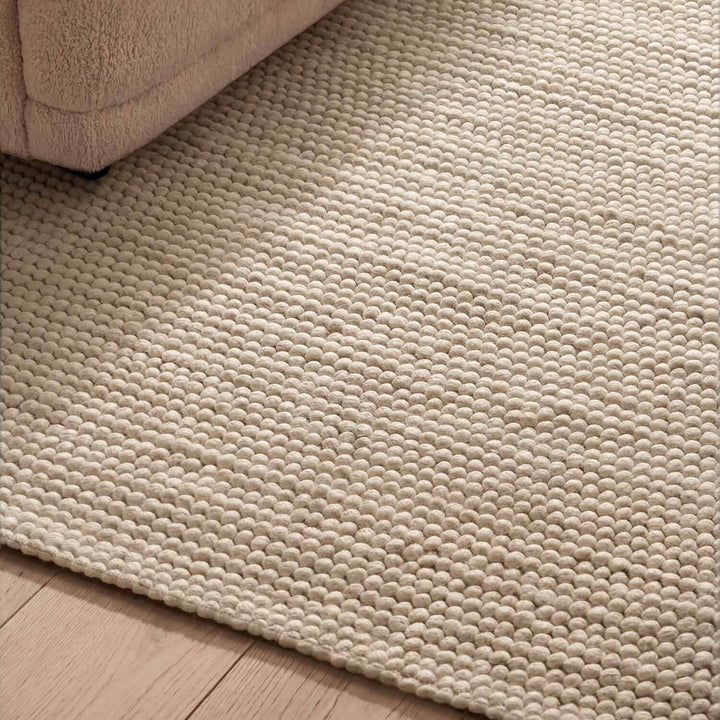 Close-up of a textured beige rug on a wooden floor