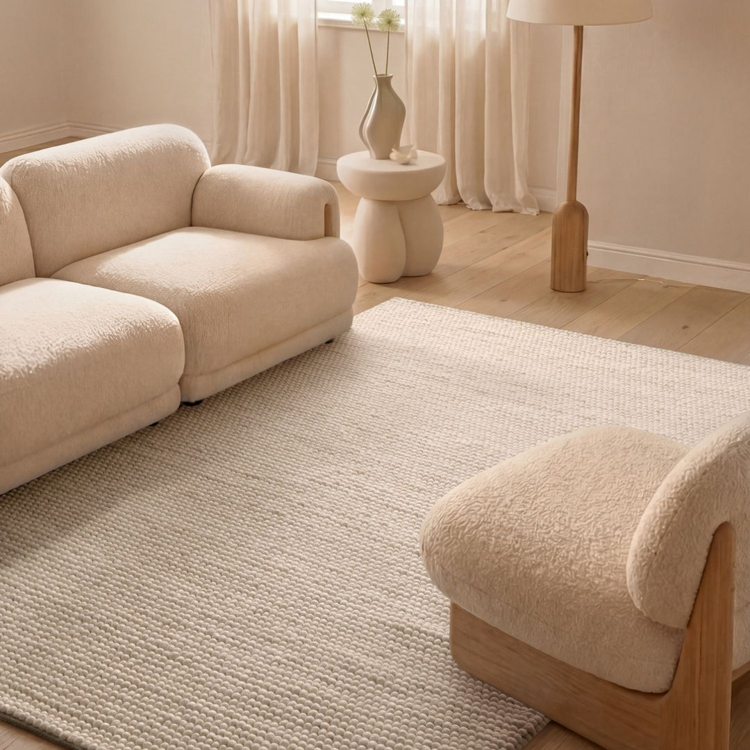 Beige sofa and armchair in a living room with a textured rug and decorative items.