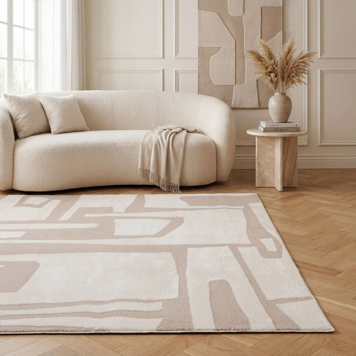 Beige living room with a modern sofa, abstract-patterned rug, and decorative elements.