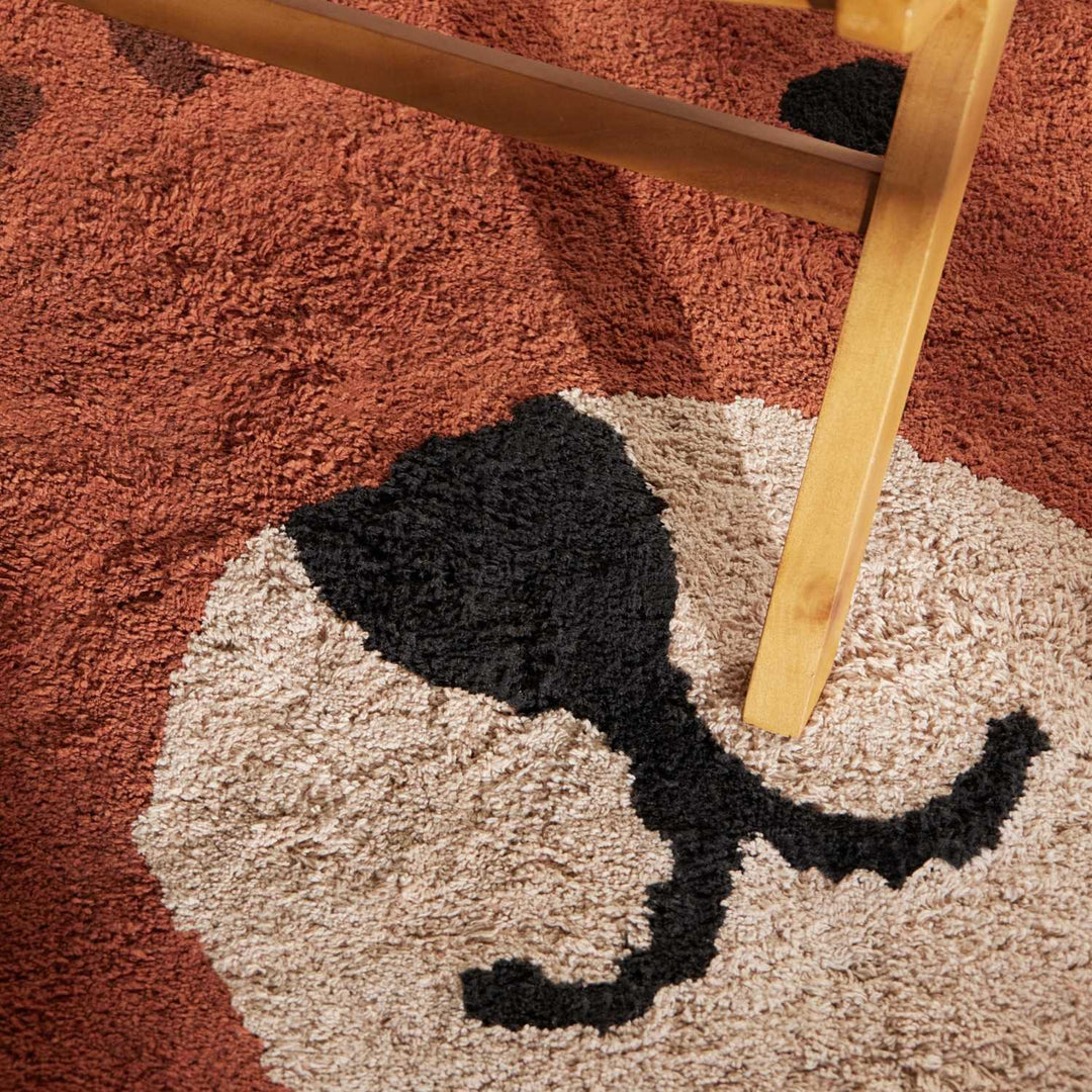 Close-up of a textured rug with a cat design and a wooden chair leg.
