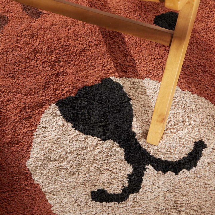 Close-up of a textured rug with a cat design and a wooden chair leg.