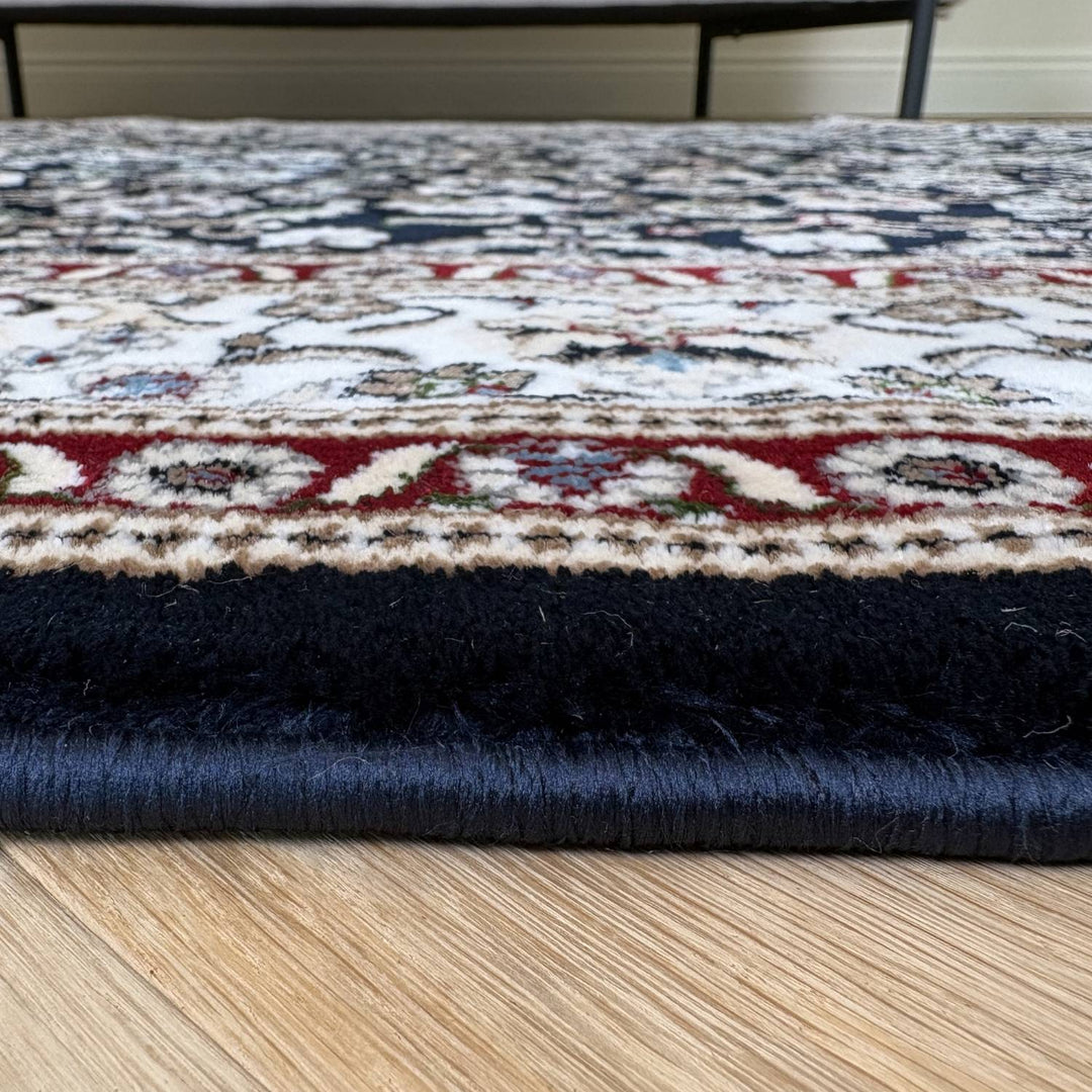 Close-up of a patterned rug with a blue border on a wooden floor.
