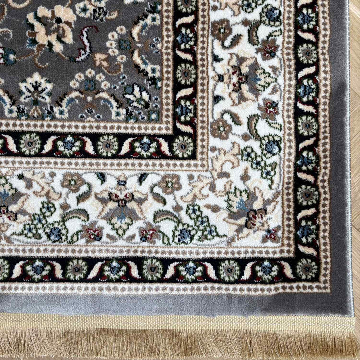 Corner of a patterned rug with intricate designs on a wooden floor.