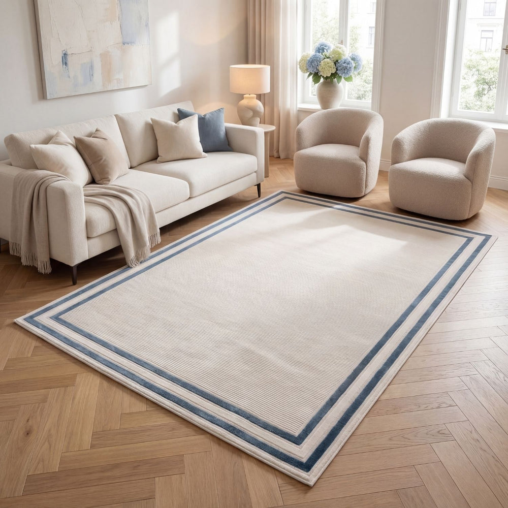 Living room with a large white rug featuring blue borders, beige sofa, and armchairs.