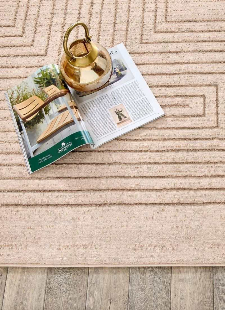 Abstract striped geometric rug in neutral tones with decorative vase and magazine on wooden floor.
