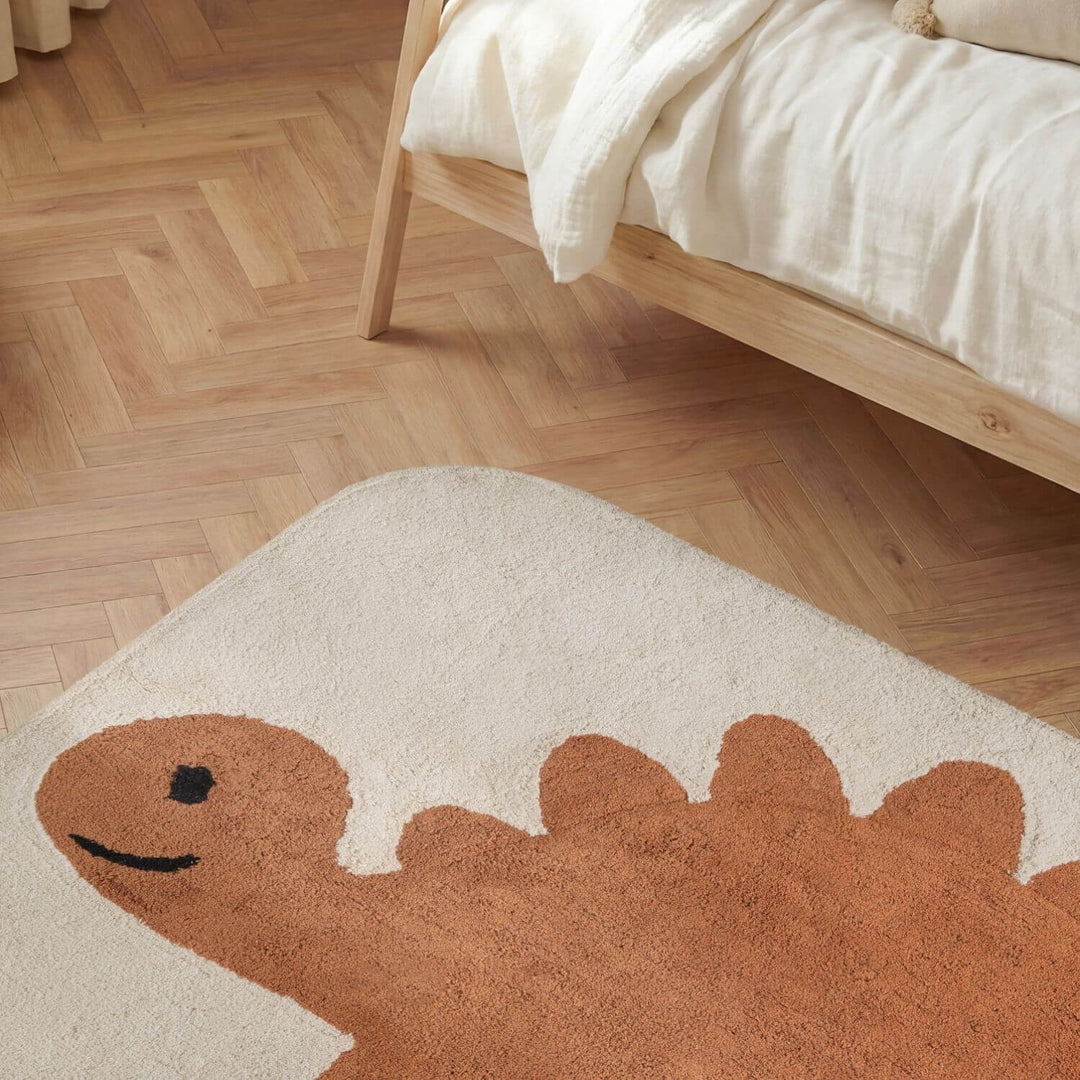 Dinosaur-shaped rug on a wooden floor next to a bed