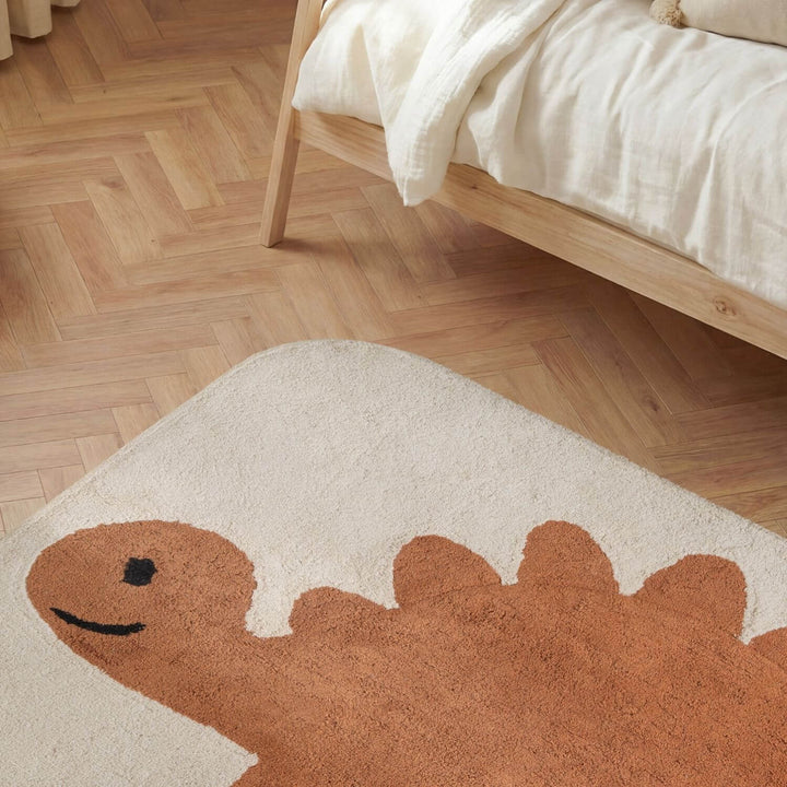 Dinosaur-shaped rug on a wooden floor next to a bed