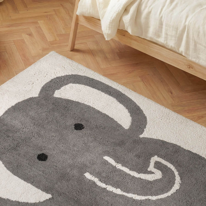 Gray elephant rug on a wooden floor next to a bed