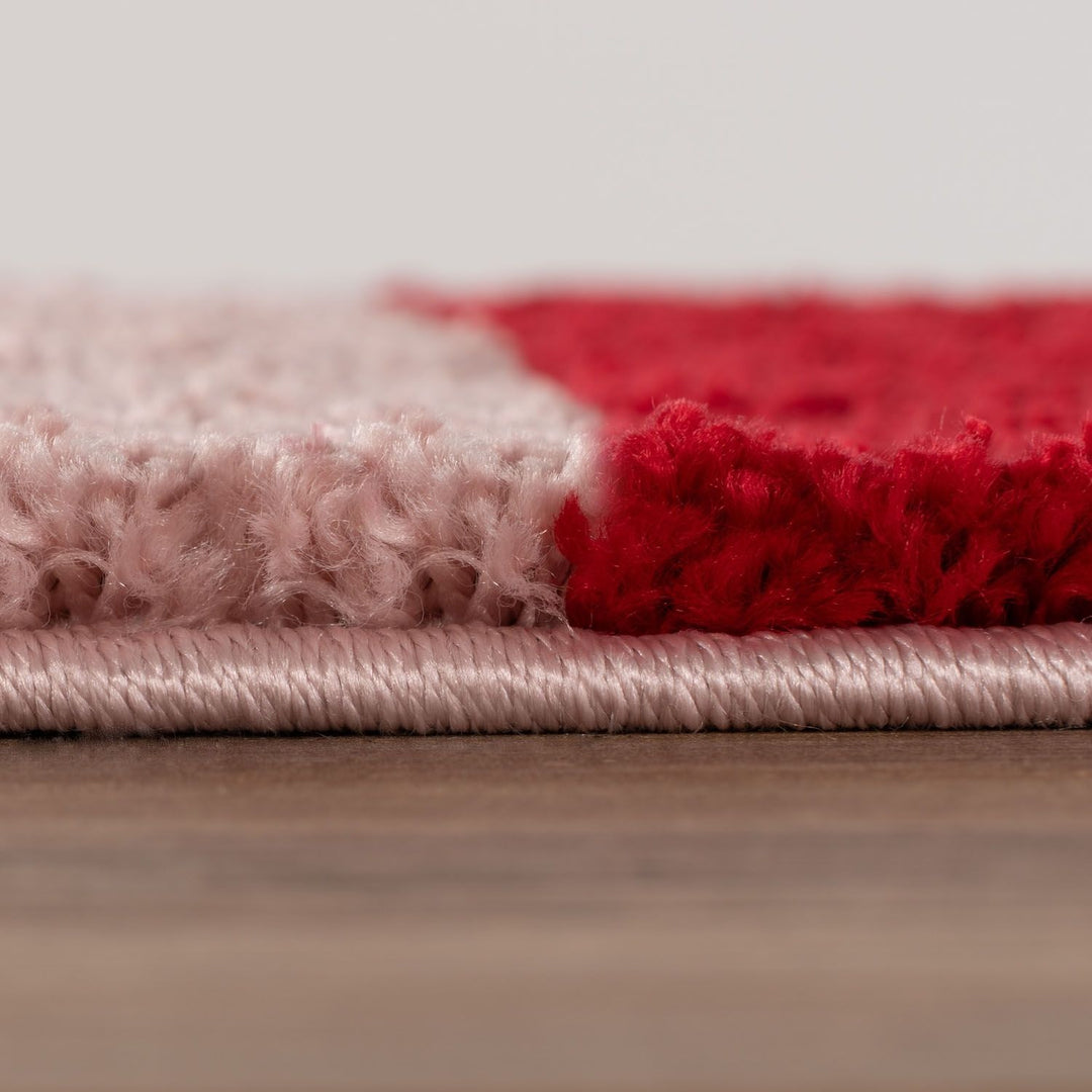Close-up of a pink and red textured rug on a wooden floor.