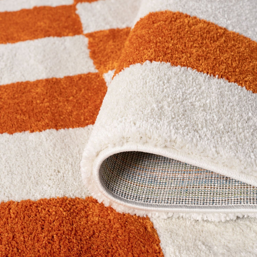Close-up of a textured orange and white striped rug with a corner turned up to reveal the backing.