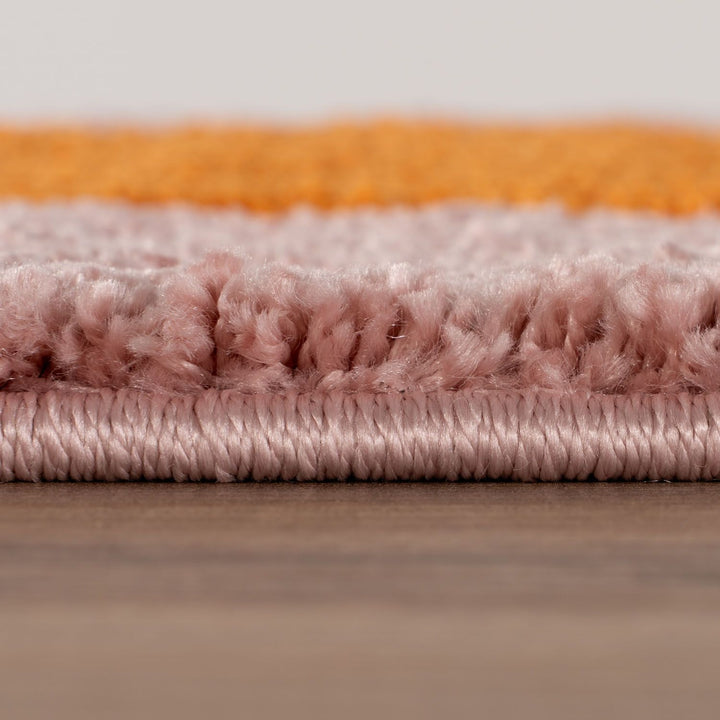 Close-up of a textured rug with orange, pink, and gray stripes on a wooden surface.