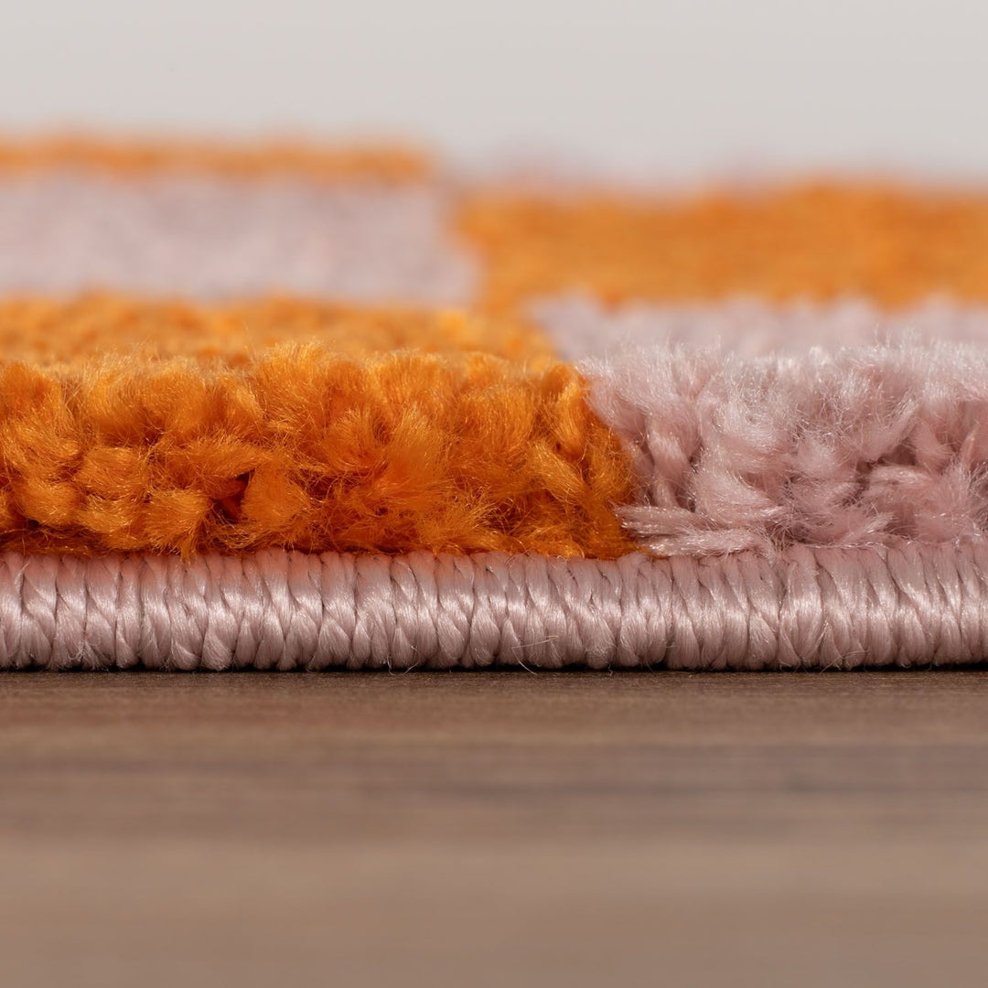 Close-up of a textured rug with orange, pink, and gray colors on a wooden floor.